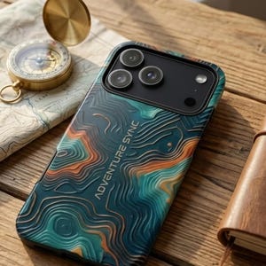 Peut inclure: Une coque de smartphone avec un motif de carte topographique dans des tons bleu sarcelle, orange et bleu foncé, avec le texte ADVENTURE SYNC en relief au dos. La coque présente une découpe pour un triple objectif photo et un flash texturé.