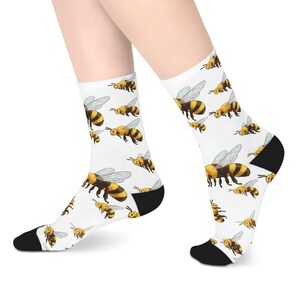 Peut inclure: Chaussettes blanches avec un motif répété d'abeilles jaunes et noires aux ailes translucides. Les chaussettes ont des talons et des orteils noirs. Les abeilles sont de tailles et d'orientations variées.