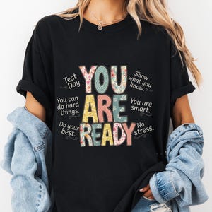 Peut inclure: T-shirt noir avec l'inscription "YOU ARE READY" en lettres colorées et à motifs. Des phrases telles que "Test Day", "You can do hard things" et "You are smart" entourent le texte principal.