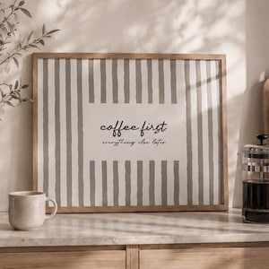 May include: A rectangular framed wall art piece featuring a vertical gray and white striped pattern with a solid white center rectangle containing the black text "coffee first everything else later" in a mix of script and sans-serif fonts.