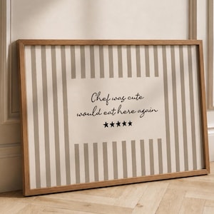 Op de afbeelding: Een rechthoekig ingelijst wandkunstwerk met een beige en witte verticaal gestreepte achtergrond. Het midden bevat een crèmekleurig rechthoekig vlak met de zwarte tekst "Chef was cute would eat here again" gevolgd door vijf zwarte sterren.