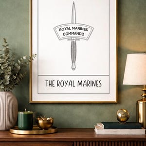 Puede incluir: Un grabado enmarcado con un marco dorado, que muestra una ilustración en blanco y negro de una daga. El texto dice "Royal Marines Commando" y "The Royal Marines". El grabado se muestra sobre una superficie de madera.