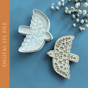 Peut inclure: Deux emporte-pièces blancs en forme d'oiseau avec des détails floraux et en forme de cœur. L'un est plein, l'autre est un contour. Ils sont sur une surface bleue avec des fleurs blanches. Le texte "DIGITAL STL FILE" est à gauche.