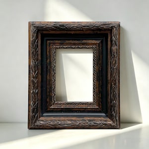Op de afbeelding: Een sierlijke, rechthoekige fotolijst met een donkerbruine, getextureerde afwerking en een zwarte binnenlijst. De lijst heeft gedetailleerde gravures langs de randen, wat een vintage uitstraling creëert. De lijst is leeg, klaar voor een foto of kunstwerk.