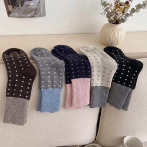 Könnte beinhalten: Fünf Paar Socken mit einem Punktemuster im oberen Bereich und einem einfarbigen Bündchen. Die Socken sind in verschiedenen Farbkombinationen erhältlich, darunter Braun, Grau, Marineblau, Creme und Schwarz mit jeweils abgesetzten Bündchen.
