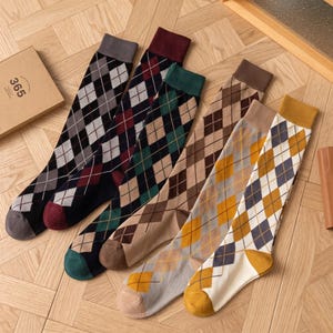 Könnte beinhalten: Ein Set aus sechs Paar kniehohen Socken mit klassischem Argyle-Rautenmuster. Die Socken sind in verschiedenen Farbkombinationen erhältlich, darunter Grau, Burgunderrot, Dunkelgrün, Braun, Beige und Gelb, jeweils mit einfarbigem Bündchen und Zehenbereich.