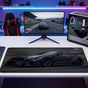May include: A gaming setup featuring a black and gray computer mouse, a black keyboard, and a computer monitor displaying a race car. A black car graphic mousepad is the focal point.