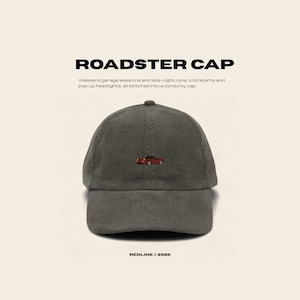 May include: A gray corduroy baseball cap with the text "ROADSTER CAP". The cap features an embroidered red car graphic. The text "REDLINE © 2026" is at the bottom. The cap is designed for weekend garage sessions and late-night runs.