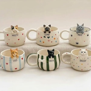 May include: Six ceramic mugs, each featuring a small, three-dimensional cat figure perched on the rim. The mugs display various patterns including hearts, flowers, paw prints, stripes, and dots, with names Misty, Luna, Meo, Leo, Onyx, and Daisy printed.