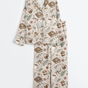 May include: Beige pajama set with a repeating pattern of books, coffee cups, eyeglasses, and flowers. The long-sleeved top has a button-down front and a notched collar. The pants are full-length, and the set is made of a soft, comfortable material.