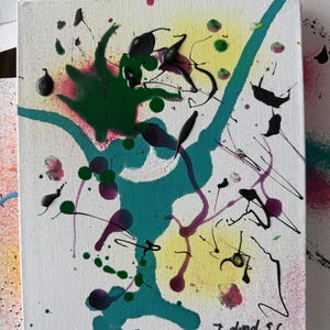 Puede incluir: Pintura de arte abstracto sobre lienzo con fondo blanco. La obra presenta salpicaduras y goteos de pintura verde, turquesa, negra, morada y rosa. La pintura tiene un degradado amarillo y rosa en el fondo. La firma del artista está en la esquina inferior derecha.