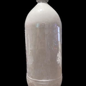Könnte beinhalten: Eine transparente Plastikflasche mit weißem Deckel, gefüllt mit einer weißen Flüssigkeit. Die Flasche hat eine abgerundete Form und einen geriffelten Boden. Der Hintergrund ist schwarz.