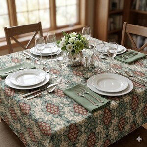 May include: A square dining table set for four with a patterned tablecloth in shades of sage green, cream, and terracotta. The table features white ceramic plates, clear glass stemware, stainless steel cutlery, and sage green cloth napkins.