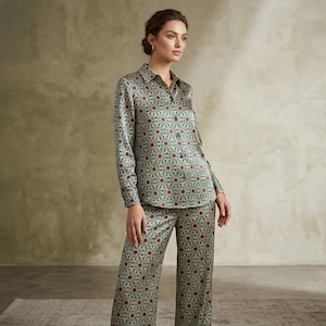 May include: A long-sleeve button-down shirt and matching wide-leg trousers featuring a repeating geometric pattern in shades of green, red, and cream. The set is crafted from a smooth, satin-like fabric with a collar and a front button closure.