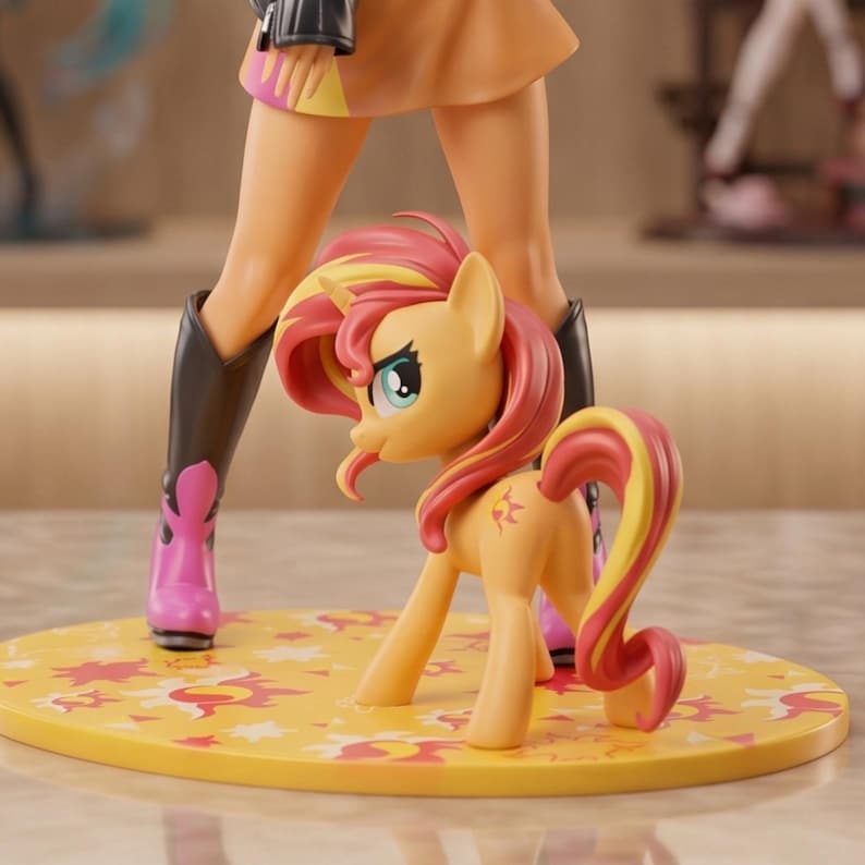 Op de afbeelding: Een verzamelfiguur van een geel pony met roze en gele manen en staart, staand op een ronde gele voet versierd met zonnesymbolen. De pony heeft een zon-teken op de flank en staat voor een mensachtig figuur.