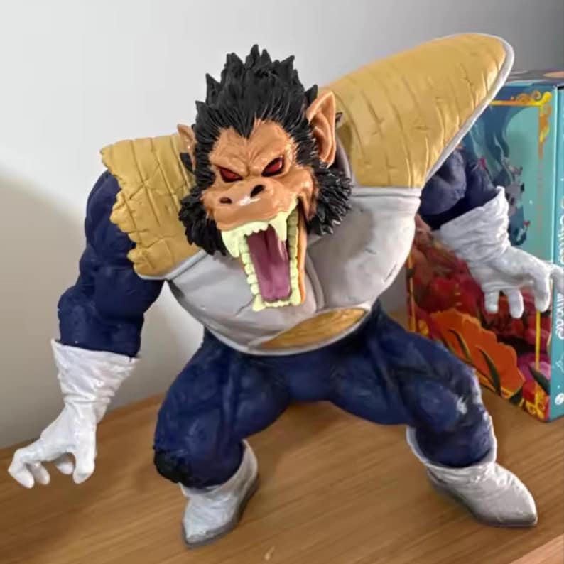 May include: A detailed figurine of a character in a dynamic pose, featuring a gorilla-like head with an open mouth, red eyes, and black fur. The figure wears a blue and white suit with gold shoulder pads and white gloves and boots. The overall design suggests a fantasy or anime theme.