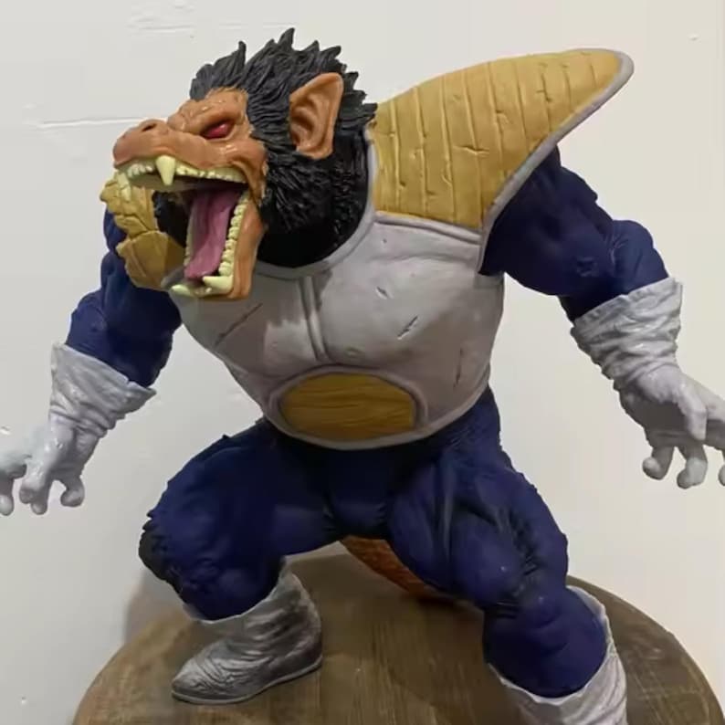 May include: A detailed figurine of a large ape-like character in a dynamic pose. The figure has a black face, tan mouth, and red eyes. It wears blue and white armour with tan shoulder pads. The figure is on a wooden base.