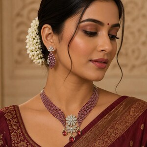 Puede incluir: Un conjunto de collar y pendientes de rubíes y diamantes. El collar presenta un colgante floral con un grupo de diamantes y tres gotas de rubí. Los pendientes tienen un diseño similar, con una forma ovalada de rubí y detalles de diamantes.