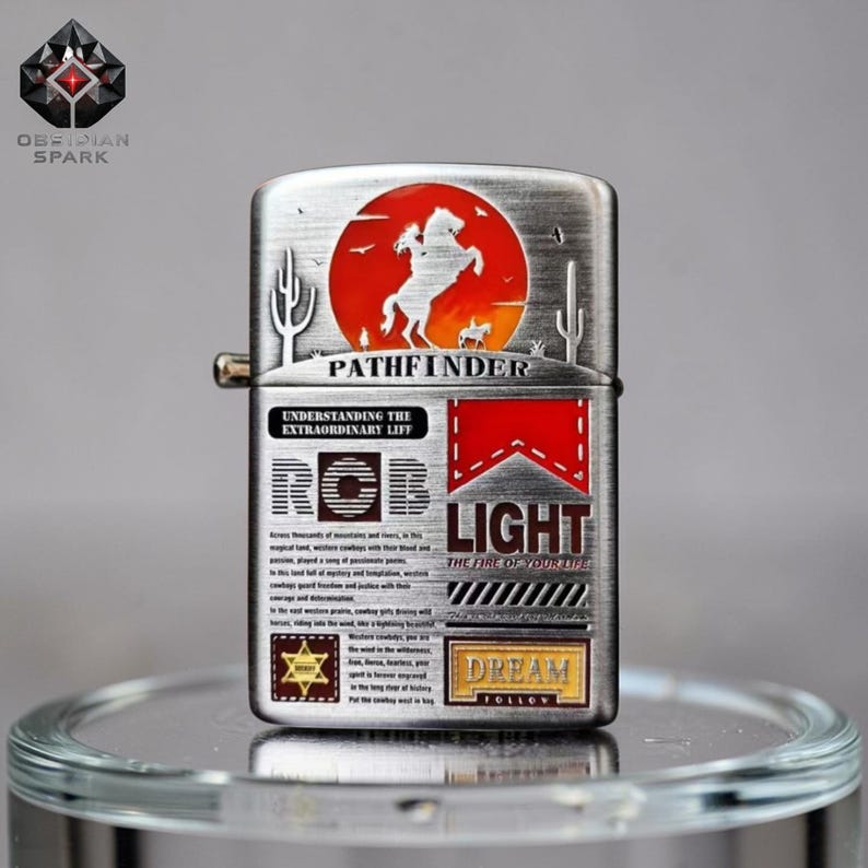 May include: A silver-toned metal lighter with a red and orange circular design featuring a horse and rider. The lighter has the word "PATHFINDER" and the text "LIGHT THE FIRE OF YOUR LIFE".