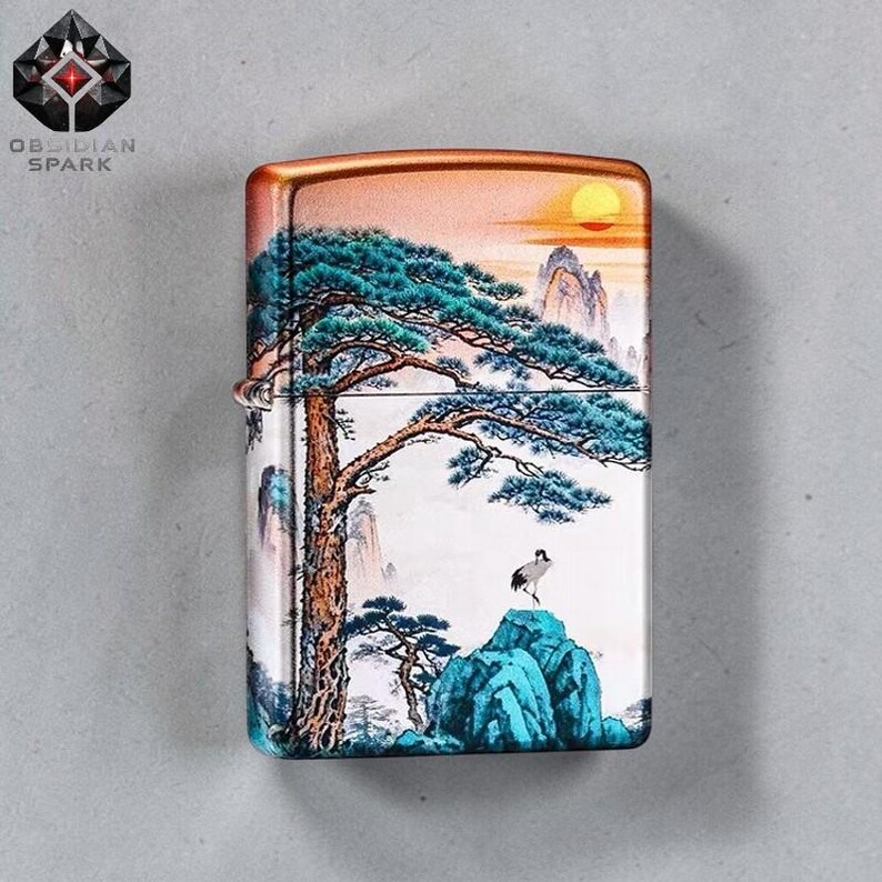 May include: A metal lighter with a landscape painting featuring a tree, mountains, and a crane. The lighter has a gold-colored top and the text "OBSIDIAN SPARK" in the upper left corner.