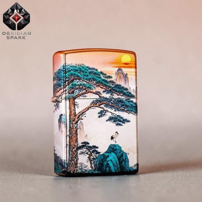 May include: A rectangular lighter with a landscape design. The artwork features a large tree with blue-green foliage, a crane, mountains, and a setting sun. The lighter has a metallic finish and the text "OBSIDIAN SPARK".