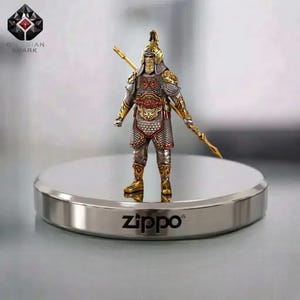 Könnte beinhalten: Detaillierte Figur eines Kriegers in kunstvoller Rüstung, der einen Speer hält. Die Figur ist überwiegend silber- und goldfarben und steht auf einer silbernen Zippo-Basis. Das Obsidian Spark-Logo ist oben links sichtbar.