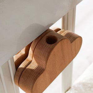 May include: A wooden cloud-shaped object with a hole, attached to a white surface. The object is made of light-colored wood and appears to be a decorative or functional item. The design is simple and natural.
