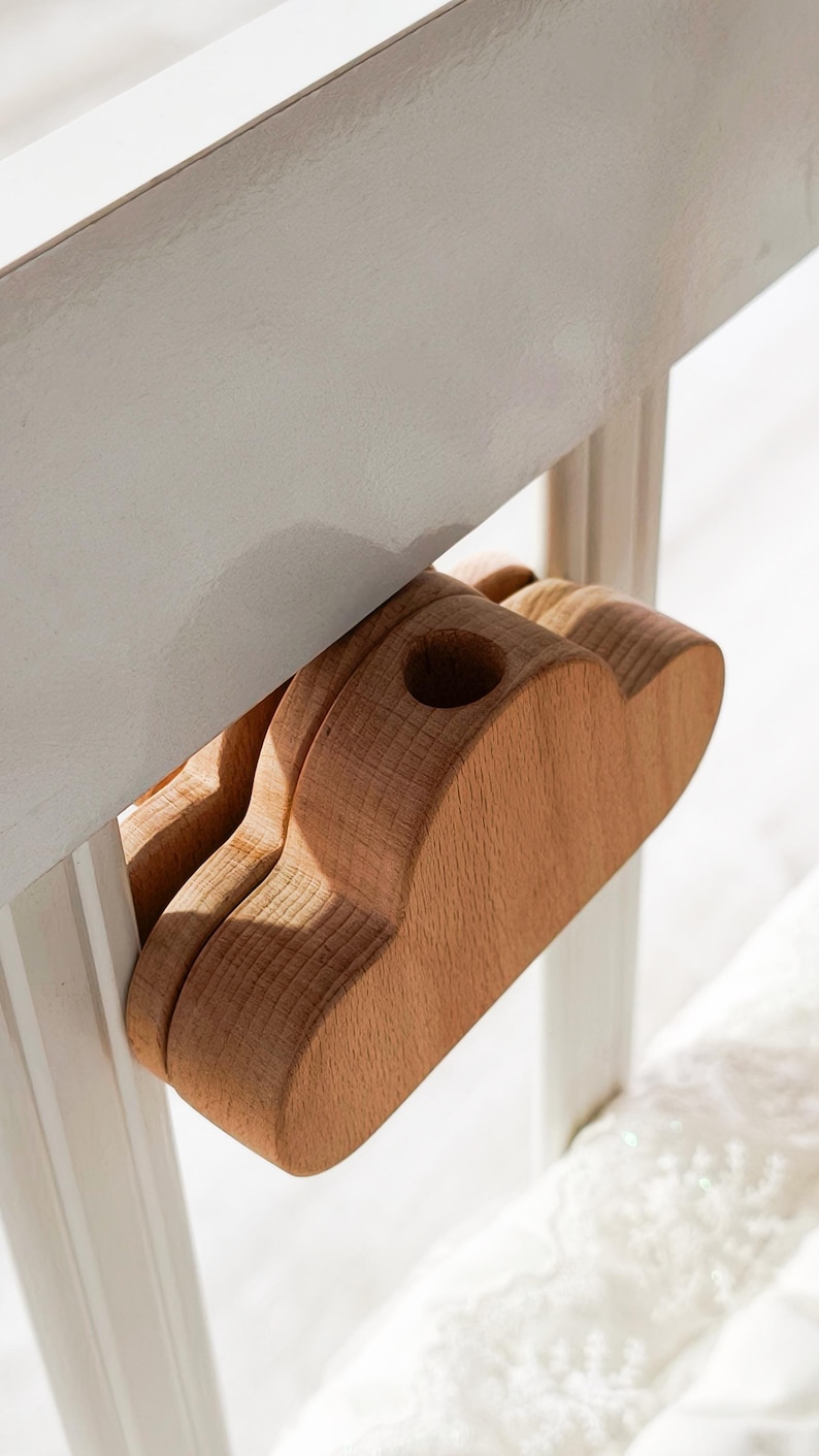 May include: A wooden cloud-shaped object with a hole, attached to a white surface. The object is made of light-colored wood and appears to be a decorative or functional item. The design is simple and natural.
