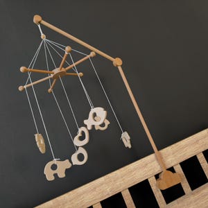 May include: A wooden baby mobile with a natural finish, featuring a central star-shaped element and hanging cut-out shapes of animals and other objects. The mobile is suspended from a wooden arm and attached to a wooden crib.