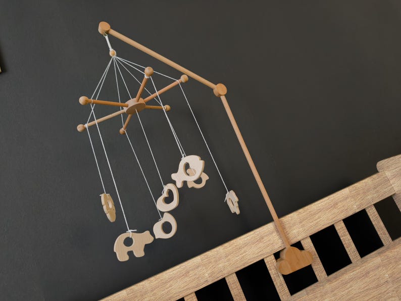 May include: A wooden baby mobile with a natural finish, featuring a central star-shaped element and hanging cut-out shapes of animals and other objects. The mobile is suspended from a wooden arm and attached to a wooden crib.