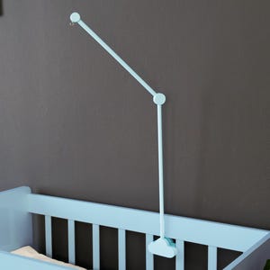 May include: A light blue baby crib with a matching mobile. The crib has a slatted design and is positioned against a dark gray wall. The mobile is attached to the wall and extends over the crib.