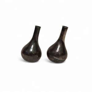 May include: Two dark gray, teardrop-shaped vases with a glossy finish. The vases have a narrow neck and a rounded base. The background is plain white.