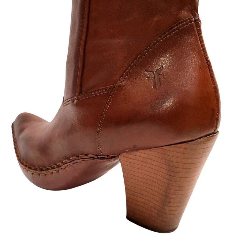 K&ouml;nnte beinhalten: Nahaufnahme eines braunen Lederstiefels mit Holzabsatz. Der Stiefel hat eine spitze Zehenpartie und eine gen&auml;hte Sohle. Das Frye-Logo ist auf der Seite des Stiefels sichtbar.