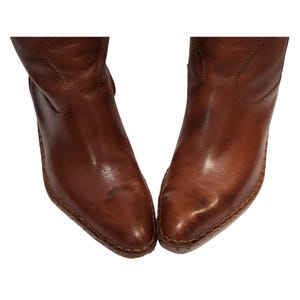 K&ouml;nnte beinhalten: Ein Paar braune Lederstiefel mit spitzer Zehenpartie. Die Stiefel haben eine mittlere Wadenh&ouml;he und einen leichten Absatz. Das Leder hat eine polierte Oberfl&auml;che und sichtbare N&auml;hte entlang der Sohlen. Die Stiefel sind vor wei&szlig;em Hintergrund.