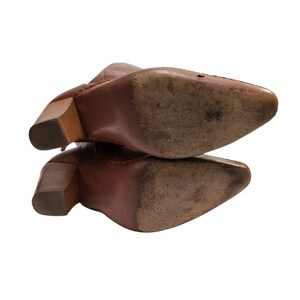 K&ouml;nnte beinhalten: Braune Lederstiefel mit spitzer Zehenpartie und Holzklotzabs&auml;tzen. Die Sohlen weisen Gebrauchsspuren auf. Die Stiefel sind angewinkelt und zeigen die Details von Absatz und Sohle vor wei&szlig;em Hintergrund. Die Stiefel scheinen Vintage zu sein.