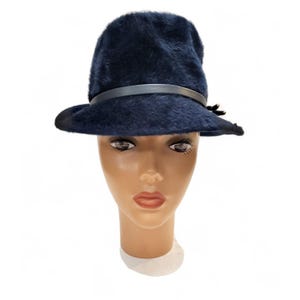 May include: A navy blue fedora hat with a dark leather band and a small decorative accent. The hat has a soft, textured appearance and a classic brim. The hat is displayed on a mannequin head.
