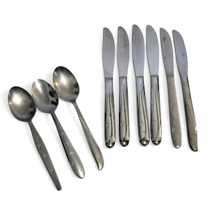 May include: A set of three silver-toned metal spoons and six silver-toned metal knives. Each piece of flatware features a slender handle decorated with small, etched starburst patterns along the lower portion of the stem.
