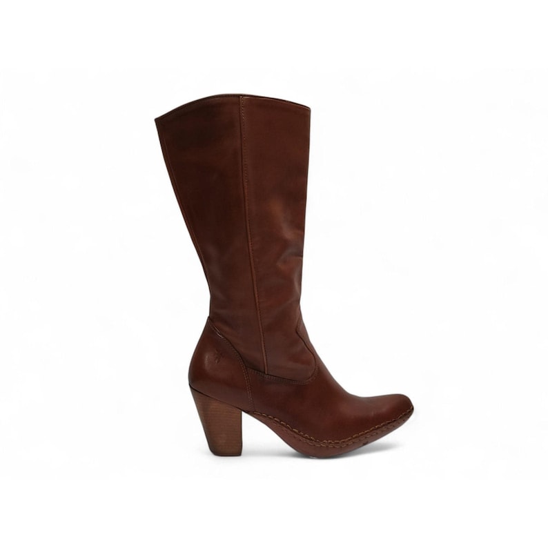 K&ouml;nnte beinhalten: Ein brauner kniehoher Lederstiefel mit einem gestapelten Holzabsatz. Der Stiefel hat eine runde Spitze und einen leicht gebogenen Schaft. Der Absatz misst ca. 7,6 cm.