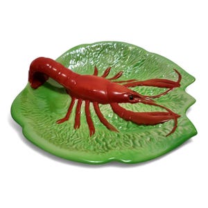 May include: A ceramic serving plate featuring a bright red lobster on a green lettuce-shaped base. The lobster has detailed claws and antennae. The plate is a decorative piece, likely for serving seafood or as a kitchen accent.
