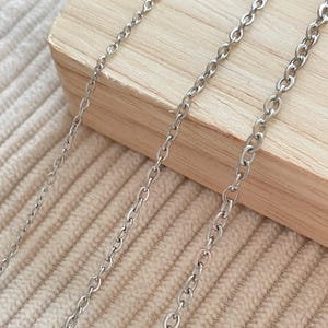 Könnte beinhalten: Nahaufnahme von drei silberfarbenen Kettenhalsketten mit unterschiedlichen Gliedergrößen. Die Ketten werden auf einer hellbeige strukturierten Oberfläche und einem Holzblock präsentiert. Das Bild enthält ein blaues und weißes Logo mit der Aufschrift "Zentro DIY Supply".