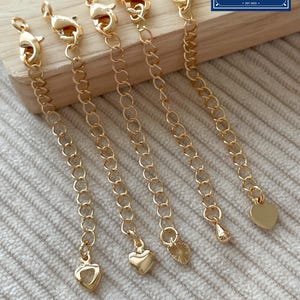 Può includere: Estensori per collana color oro con chiusure a moschettone e ciondoli a forma di cuore. Gli estensori sono costituiti da piccole catene collegate. L'immagine include anche un logo che dice "Zentro DIY Supply".