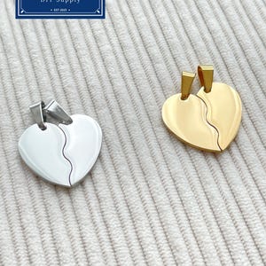 Op de afbeelding: Twee hartvormige hangers, één zilverkleurig en één goudkleurig, elk in het midden gesplitst. De hangers liggen op een getextureerd, gebroken witte ondergrond. In de linkerbovenhoek staat een blauw-wit logo met "Zentro DIY Supply".