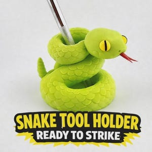May include: A bright lime green coiled snake tool holder with yellow eyes and a red tongue, featuring a metallic tool inserted into its top. Below the snake, the text reads SNAKE TOOL HOLDER READY TO STRIKE in bold black and yellow lettering.