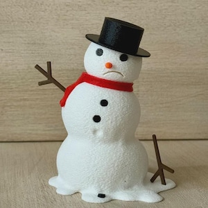 May include: A white snowman figurine with a textured surface, wearing a black top hat and a red scarf. It features two black eyes, an orange carrot-shaped nose, a sad mouth, and two black buttons on its chest. Brown stick-like arms extend outward.