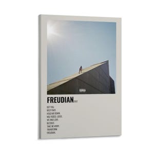 May include: A framed art print featuring a photograph of a person walking on a building's rooftop under a bright sky. The print has the word "FREUDIAN" and the year "2017" printed on it, along with a list of song titles.