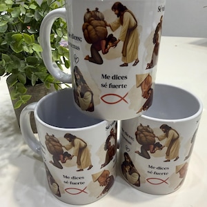May include: White ceramic mugs stacked, each featuring a religious illustration. The design includes figures in robes, text in Spanish, and a fish symbol. The mugs have a handle and a light blue interior.