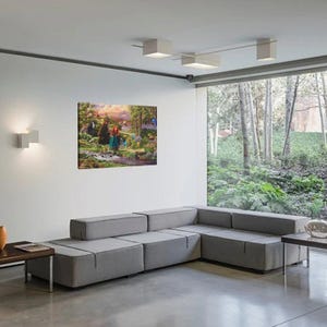 May include: A framed canvas art print depicting a colorful scene with characters in a forest setting. The artwork features a woman with red hair and a bear. The print is displayed on a white wall above a gray sectional sofa.