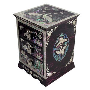 May include: A dark wood jewelry box with four drawers, decorated with mother-of-pearl inlay. The top features cranes and floral designs. The drawers have butterfly-shaped handles and floral accents. The sides have crane and floral designs.
