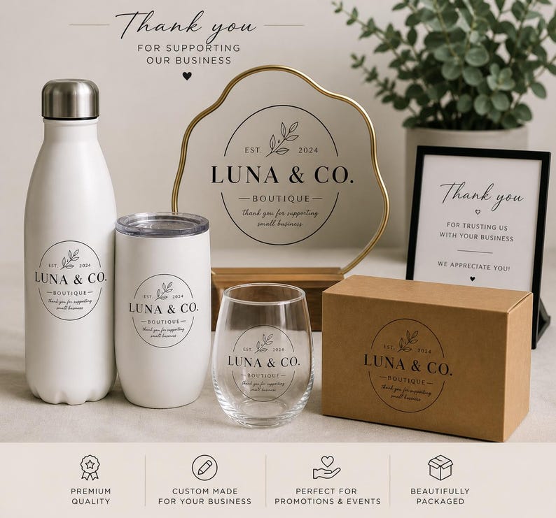 May include: White water bottle, tumbler, and stemless wine glass with the "LUNA & CO. Boutique" logo. A gold-rimmed sign and a framed "Thank you" sign are also visible. A brown box with the same logo is also present.
