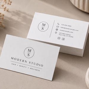 May include: A stack of white rectangular business cards featuring a black circular logo with the letters MS. The front card displays the text MODERN STUDIO, HAIR, BEAUTY, WELLNESS. The back card shows contact details including a phone number, email, website, address, and social media icons.
